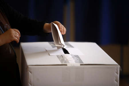Hand of a person casting a ballot at a polling station during voting.