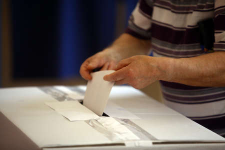 Hand of a person casting a ballot at a polling station during voting.