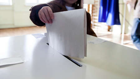 Hand of a person casting a ballot at a polling station during voting.