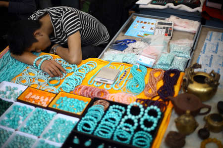Beijing, China - September 24, 2014: A man falls asleep while selling jewelry in a market in Beijing, China.のeditorial素材