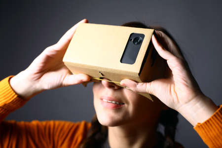 Color shot of a young woman looking through a cardboard, a device with which one can experience virtual reality on a mobile phone.のeditorial素材
