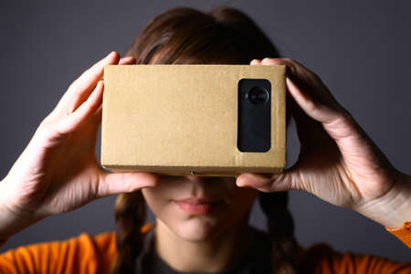 Color shot of a young woman looking through a cardboard, a device with which one can experience virtual reality on a mobile phone.の写真素材
