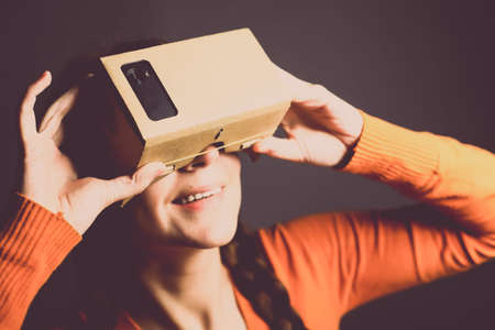 Color shot of a young woman looking through a cardboard, a device with which one can experience virtual reality on a mobile phone.の写真素材