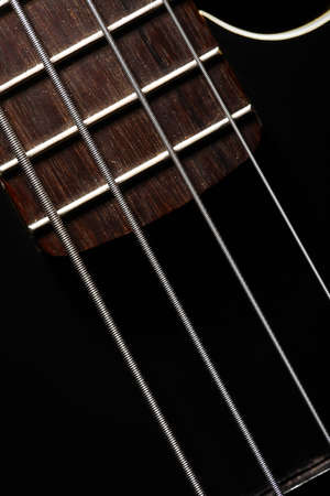 Horizontal detail of the fret board of a bass guitar, on a dark background.
