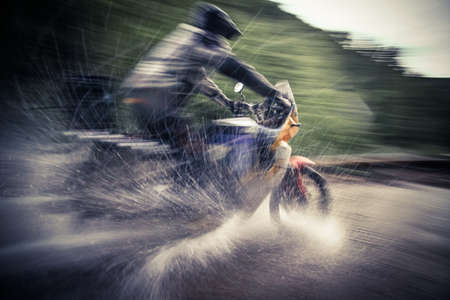 Color shot, blurred motion, of a motorcyclist crossing a river.の写真素材