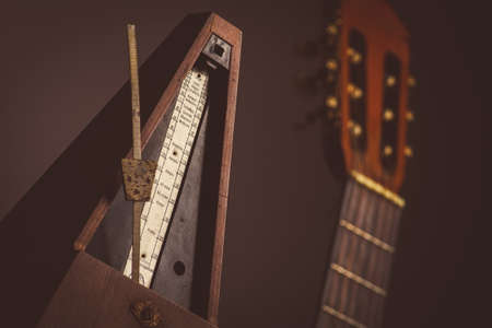 Color shot of a vintage metronome, next to an acoustic guitar, on a black background.の写真素材