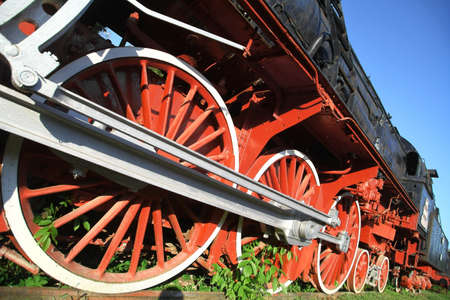 Color image of an abandoned steam locomotive's wheels, with plants growing around them.
