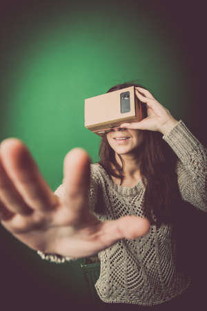 Color shot of a young woman looking through a cardboard, a device with which one can experience virtual reality on a mobile phone.の写真素材