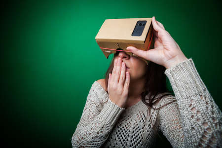Color shot of a young woman looking through a cardboard, a device with which one can experience virtual reality on a mobile phone.の写真素材