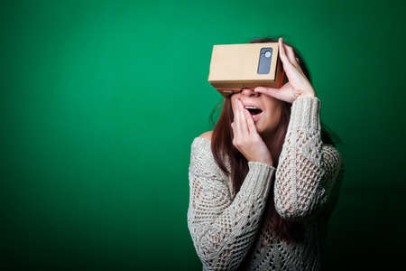 Color shot of a young woman looking through a cardboard, a device with which one can experience virtual reality on a mobile phone.の写真素材