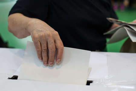 Hand of a person casting a ballot at a polling station during voting.