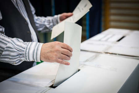 Hand of a person casting a ballot at a polling station during voting.