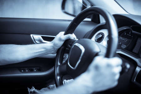 Close up shot of a man's hands holding a car's steering wheel.
