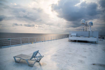 Color image of a beach chair lounger on the deck of a ship, under a dramatic cloudy sky.の写真素材