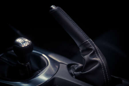 Close up shot of a parking brake lever and gear shifter inside a car.
