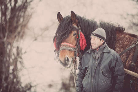 Pietrosani, Romania - January 6, 2017: A man stands near a horse in Pietrosani, Romania.のeditorial素材