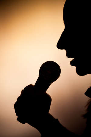 Close up image of a silhouette of a woman singing to a microphone.の写真素材