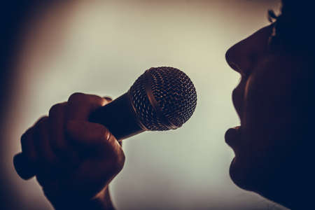 Close up image of a silhouette of a woman singing to a microphone.
