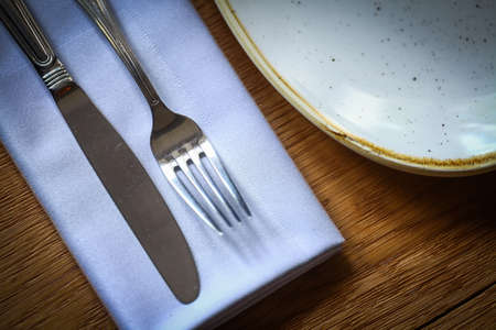 Close up shot of a fork and knife on a wooden table, on a napkin, near an empty plate.の写真素材