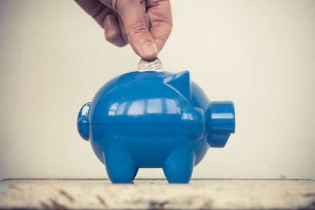 Color image of a blue piggy bank and a person adding coins.の写真素材