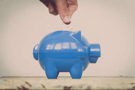 Color image of a blue piggy bank and a person adding coins.の写真素材