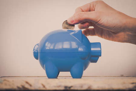Color image of a blue piggy bank and a person adding coins.の写真素材