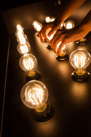 People touch light bulbs displayed on a table.