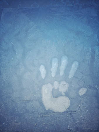 Close up shot of a human palm imprint on a frosty window.
