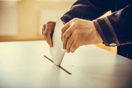 Color image of a person casting a ballot at a polling station, during elections.