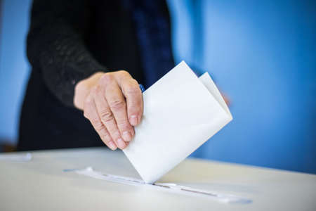 Color image of a person casting a ballot at a polling station, during elections.