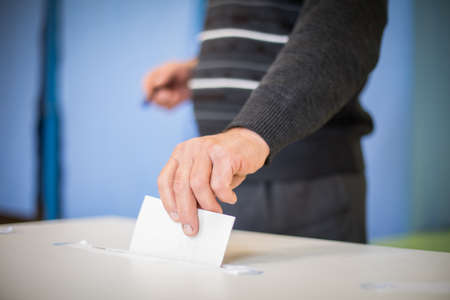 Color image of a person casting a ballot at a polling station, during elections.