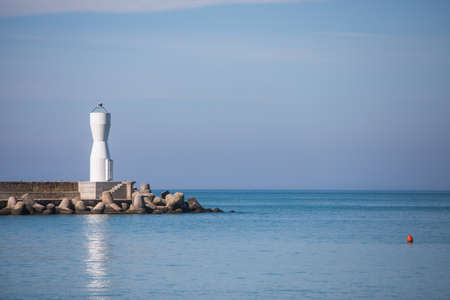 A modern white lighthouse is pictured against a blue sky, by the sea.の写真素材