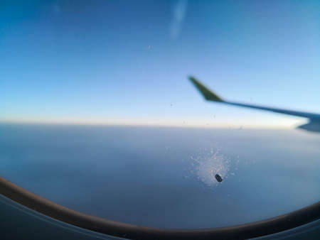 Color close up shot of a little hole in the window of a passenger airplane, flying above the clouds.