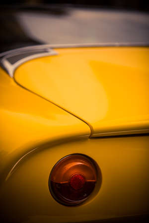 Close up vertical image of the red tail light of a yellow classical vintage car.