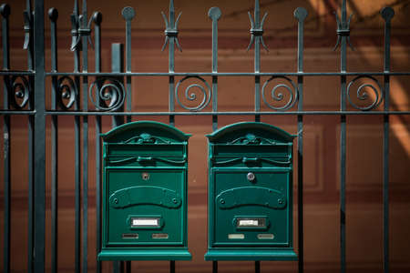 Two vintage green mail boxes on a fence.