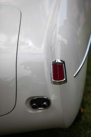 Close up vertical image of the red tail light and exhaust pipes of a white classical vintage car.