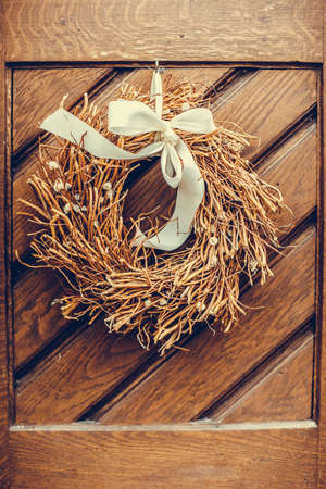 Color close up shot of dried wreath made of plants hanging on a wooden door.の写真素材