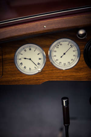 Color close up shot of a tachometer and a clock on a vintage car's dashboard.