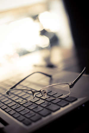 Close up shot of a pair of glasses on a laptop keyboard, with shallow depth of field.の写真素材