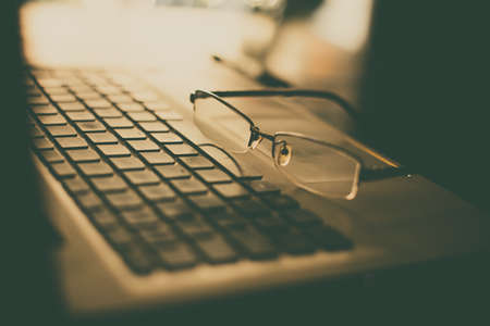 Close up shot of a pair of glasses on a laptop keyboard, with shallow depth of field.の写真素材