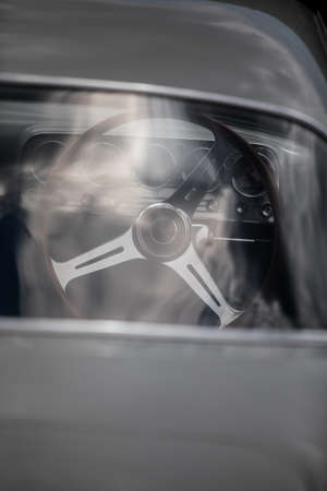 Color close up of the wooden steering wheel of an old classic car seen through the rear window.