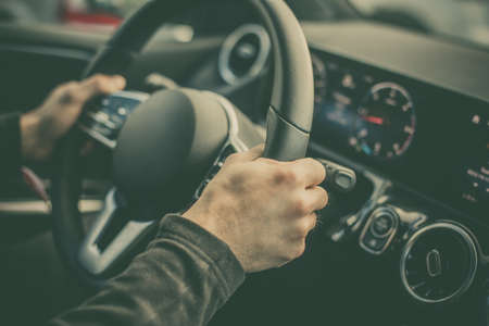 Close up shot of a man's hand holding the steering wheel while driving a modern car.