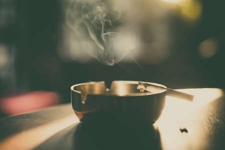 Close up shot of a burning cigarette in an ashtray, with smoke rising.の写真素材