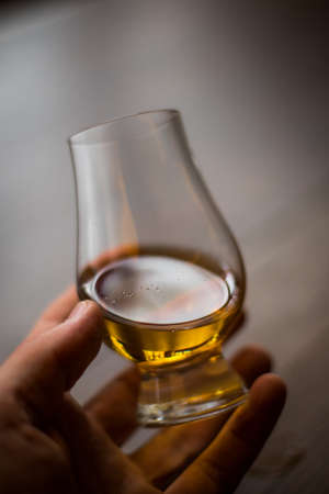 Close up shot of a hand holding a Glencairn whisky glass.