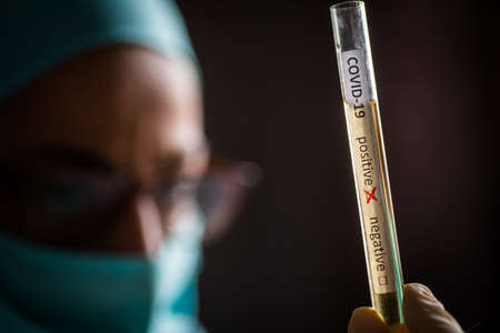 Conceptual photograph of a doctor's hands holding and looking at a test tube while with positive...