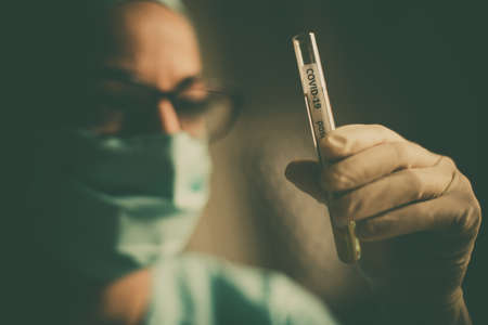 Conceptual photograph of a doctor holding and looking at a test tube while testing samples for presence of coronavirus (COVID-19).の写真素材