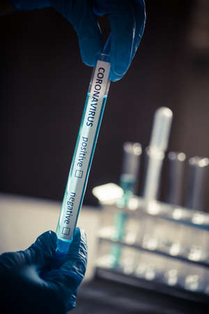 Conceptual photograph of a hand holding and looking at a test tube while testing samples for...