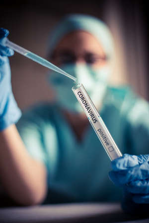 Conceptual photograph of a doctor taking samples from a test tube with a pipette, while testing for presence of coronavirus (COVID-19).の写真素材