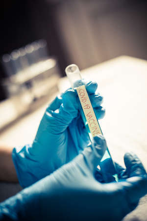 Conceptual image of a doctor holding and looking at a tube of coronavirus (COVID-19) vaccine.
