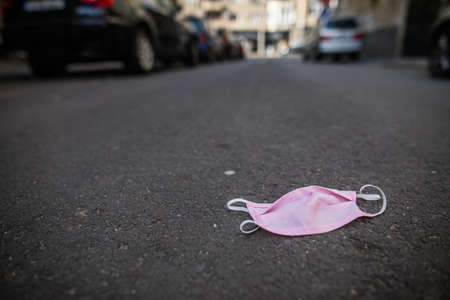 A used pink face protection mask lies abandoned on the pavement.の写真素材